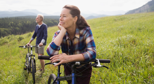 Middle aged woman with partner in the background taking a break on a hill during a bike ride